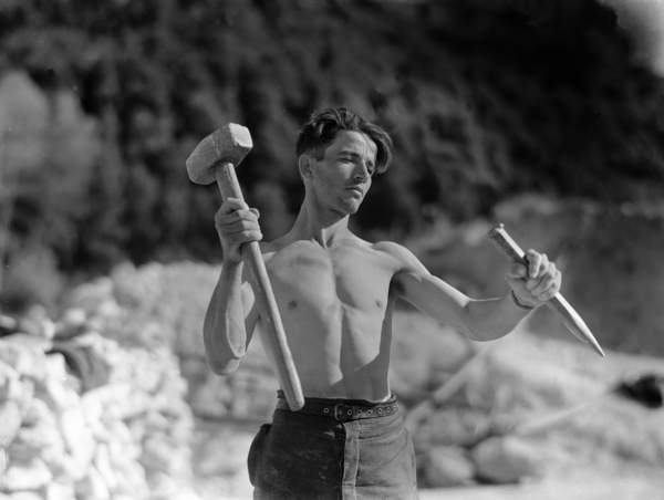 a bare-chested young worker with mallet and a chisel in Laconi Cave, Italy 1940-50 (b/w photo)